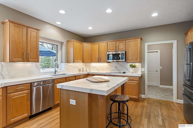 kitchen with stainless steel appliances, backsplash, a sink, a kitchen island, and light wood-type flooring