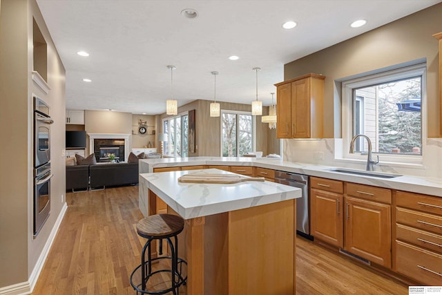 kitchen featuring a peninsula, a sink, open floor plan, appliances with stainless steel finishes, and a glass covered fireplace