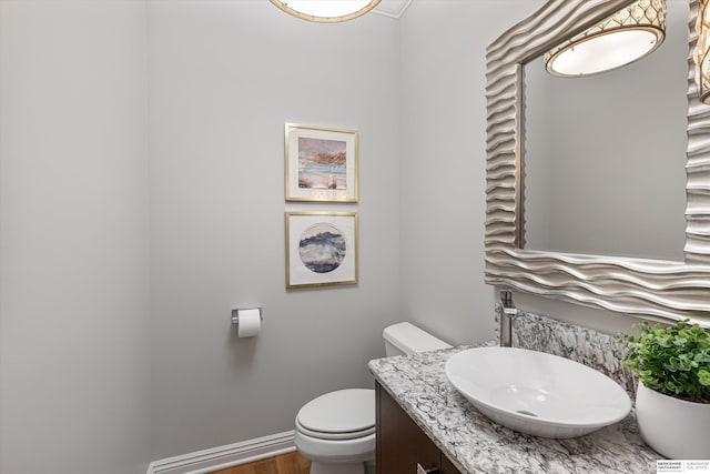 half bath featuring wood finished floors, vanity, toilet, and baseboards