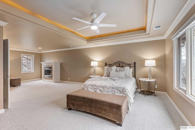 carpeted bedroom featuring crown molding, a glass covered fireplace, a raised ceiling, and baseboards