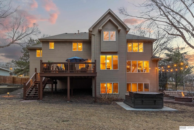 back of house at dusk featuring a hot tub, a fire pit, stairs, fence, and a wooden deck