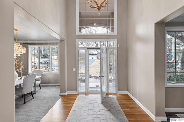 entrance foyer with wood finished floors, a towering ceiling, baseboards, and an inviting chandelier