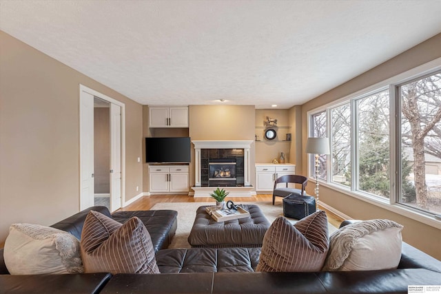 living area featuring light wood finished floors, a textured ceiling, baseboards, and a tiled fireplace