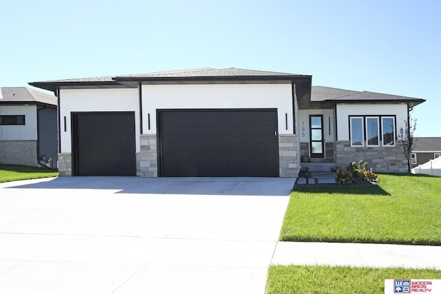 prairie-style house featuring a garage, stone siding, a front lawn, and concrete driveway