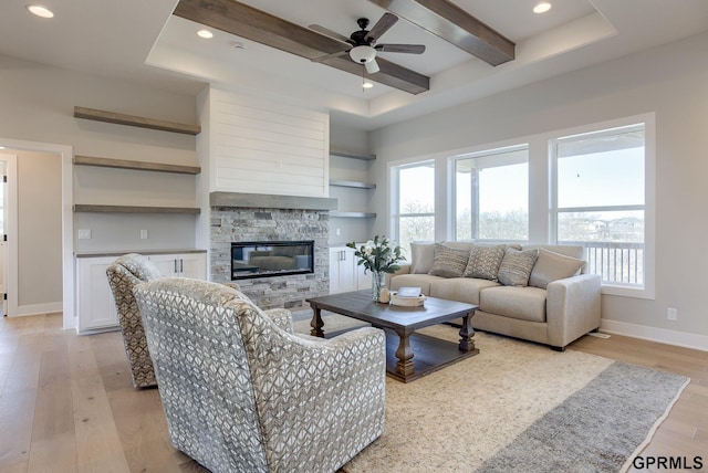 living room with baseboards, beamed ceiling, a stone fireplace, light wood-type flooring, and recessed lighting