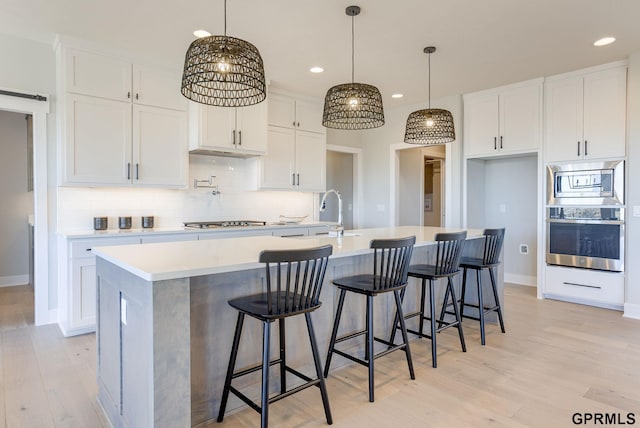 kitchen with light countertops, a center island with sink, a sink, and white cabinetry