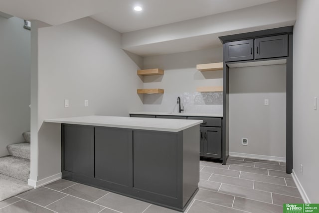 kitchen with open shelves, light countertops, a sink, a peninsula, and baseboards