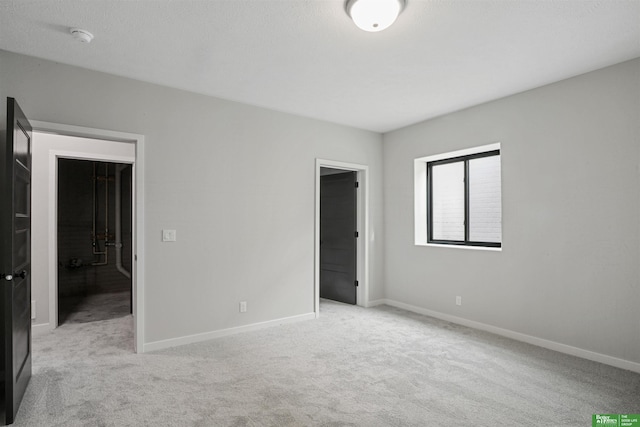 unfurnished bedroom featuring light carpet, a textured ceiling, and baseboards