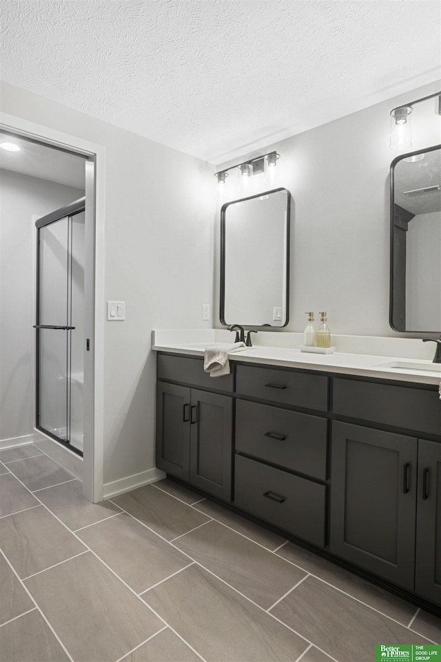 bathroom featuring double vanity, a shower stall, a textured ceiling, and a sink