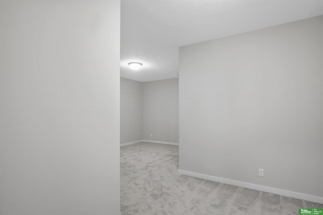 empty room featuring light carpet, a textured ceiling, and baseboards