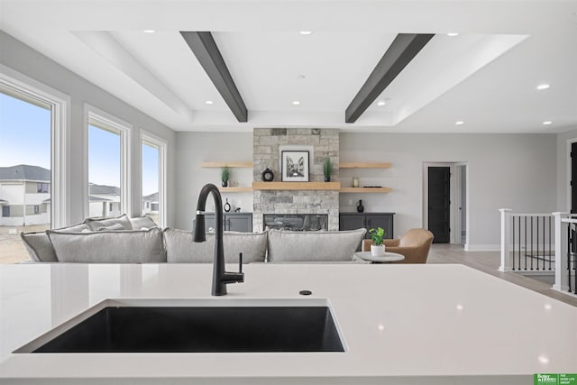 kitchen featuring a fireplace, light countertops, open floor plan, a sink, and beamed ceiling