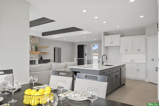 kitchen with a sink, white cabinetry, stainless steel dishwasher, decorative backsplash, and light wood finished floors