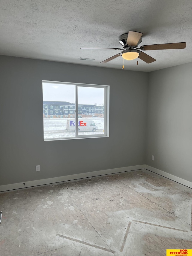 spare room with a ceiling fan, a view of city, baseboards, and a textured ceiling