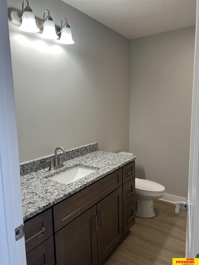 bathroom featuring toilet, a textured ceiling, vanity, wood finished floors, and baseboards