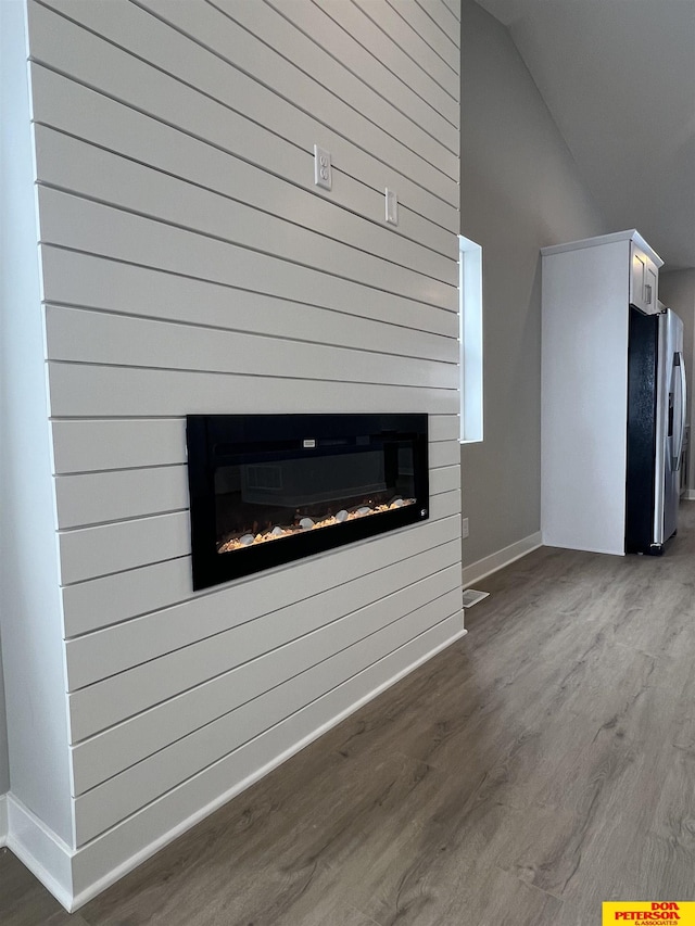 unfurnished living room featuring dark wood-style floors, baseboards, a glass covered fireplace, and lofted ceiling