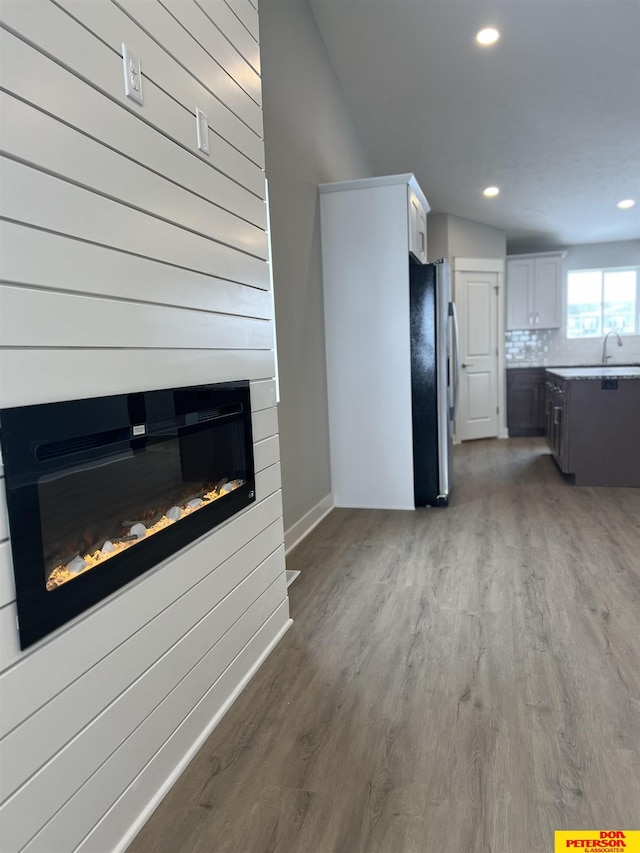 unfurnished living room featuring recessed lighting, a large fireplace, a sink, wood finished floors, and baseboards