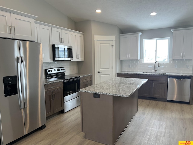 kitchen with appliances with stainless steel finishes, light stone counters, a center island, white cabinetry, and a sink