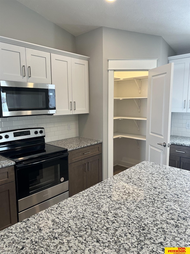 kitchen with stainless steel appliances, white cabinetry, dark brown cabinetry, and backsplash