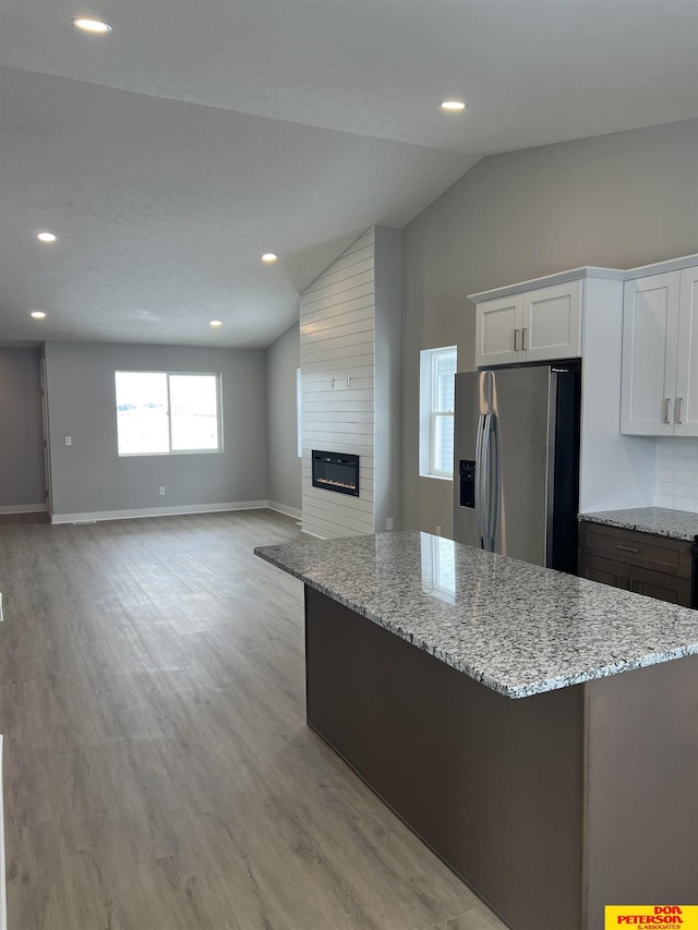 kitchen with stainless steel fridge, white cabinetry, open floor plan, and light stone counters