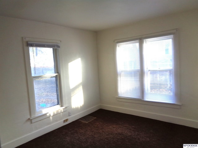 spare room with baseboards, visible vents, and dark carpet