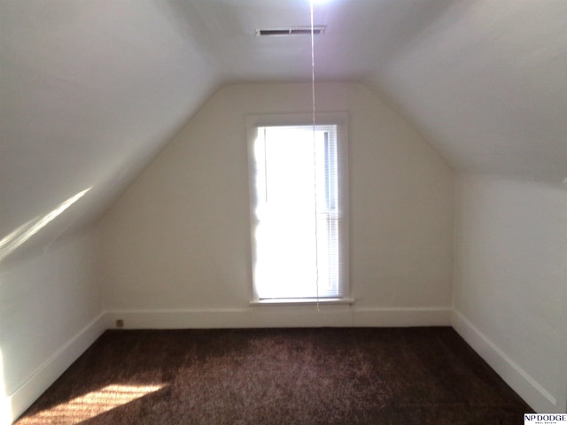 additional living space with vaulted ceiling, dark carpet, visible vents, and baseboards