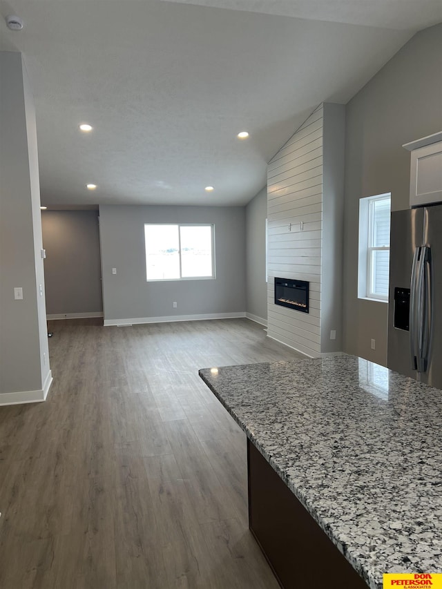 unfurnished living room with light wood finished floors, baseboards, lofted ceiling, a fireplace, and recessed lighting