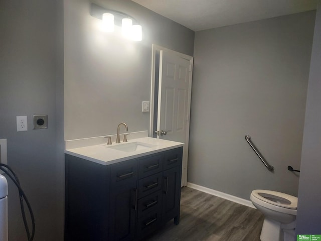 bathroom with toilet, wood finished floors, vanity, and baseboards