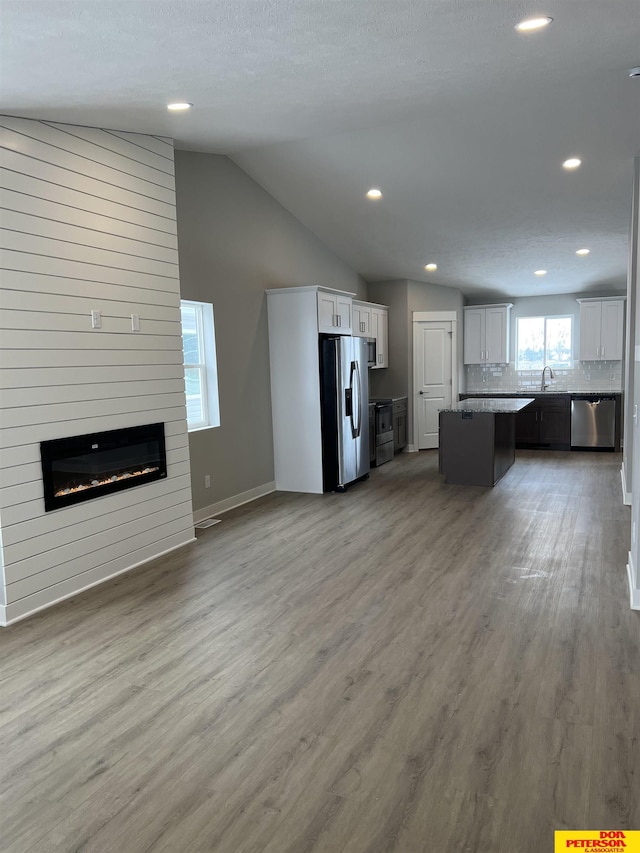 unfurnished living room featuring a large fireplace, lofted ceiling, light wood-style floors, a sink, and recessed lighting