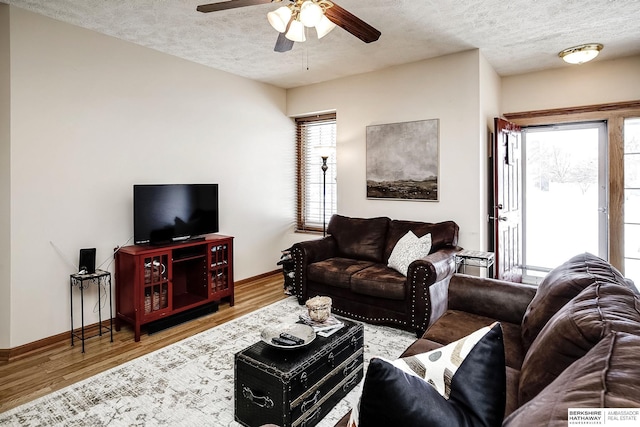 living room with a textured ceiling, a ceiling fan, baseboards, and wood finished floors