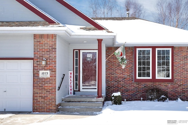 snow covered property entrance featuring brick siding and an attached garage