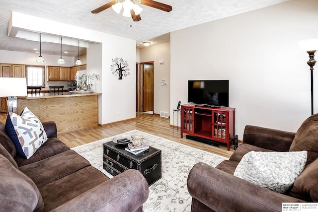 living room with a textured ceiling, a ceiling fan, baseboards, visible vents, and light wood-style floors