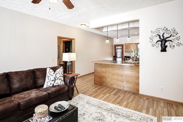 living area featuring baseboards, light wood-style floors, a ceiling fan, and a textured ceiling