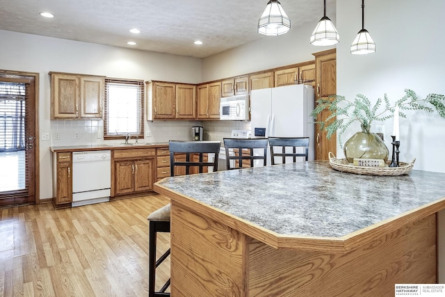 kitchen featuring white appliances, a sink, decorative backsplash, a kitchen breakfast bar, and light wood-type flooring