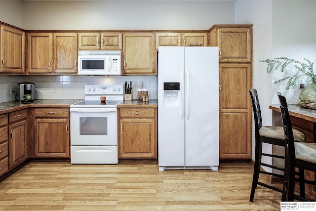 kitchen featuring decorative backsplash, white appliances, brown cabinets, and light wood finished floors