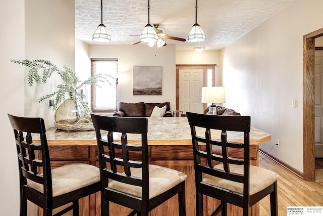 dining space with ceiling fan, baseboards, light wood-type flooring, and a textured ceiling