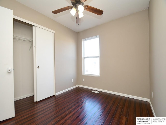 unfurnished bedroom featuring dark wood-style flooring, a closet, visible vents, and baseboards