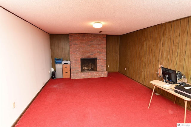 carpeted home office with a textured ceiling, wood walls, and a brick fireplace