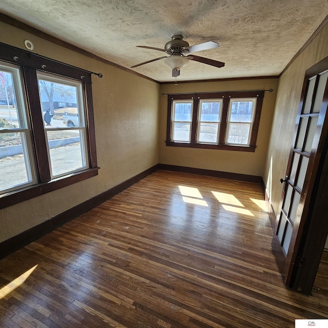 empty room featuring a healthy amount of sunlight, a textured ceiling, dark wood-style flooring, and crown molding