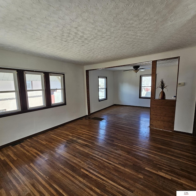 empty room featuring a textured ceiling, dark wood-type flooring, a ceiling fan, and baseboards