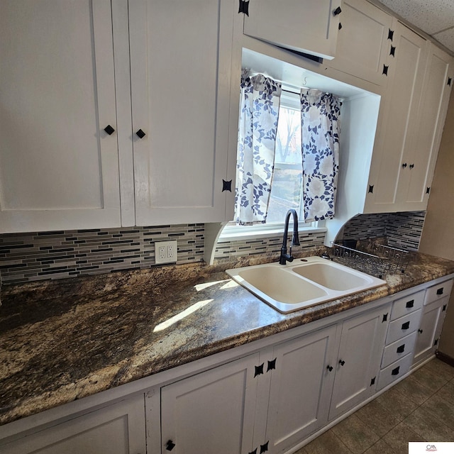 kitchen featuring dark stone countertops, tasteful backsplash, white cabinetry, and a sink