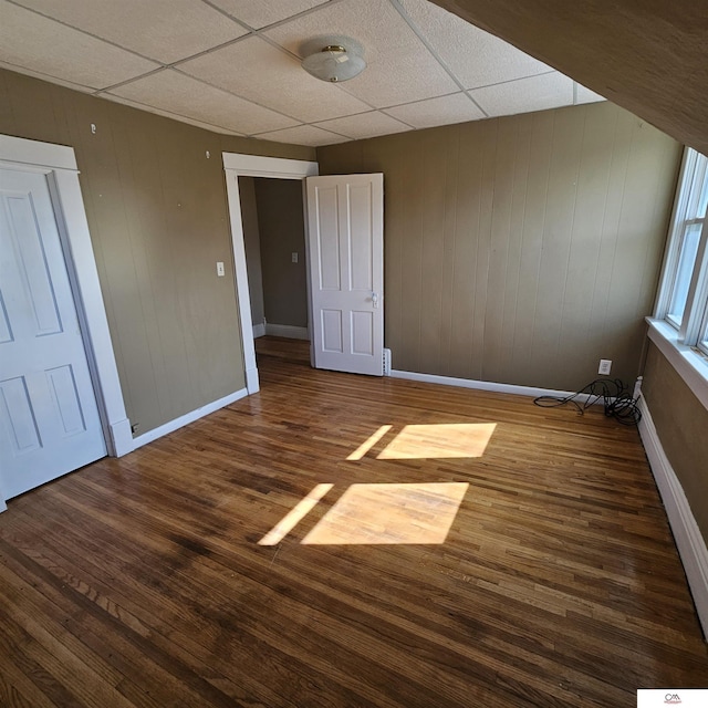 unfurnished bedroom featuring dark wood-style floors, a paneled ceiling, and baseboards