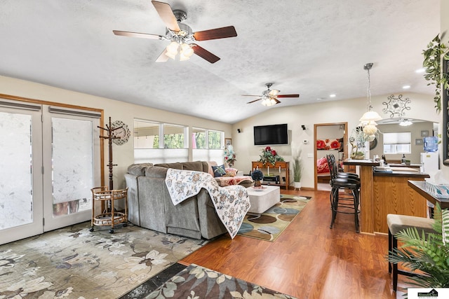 living area featuring vaulted ceiling, a textured ceiling, wood finished floors, and a ceiling fan