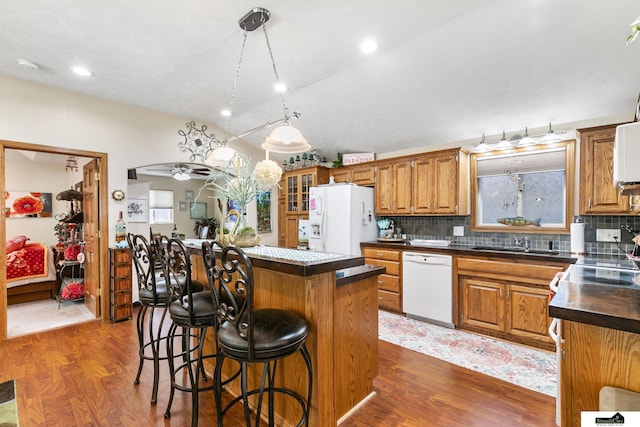 kitchen with brown cabinetry, a center island, white appliances, and dark wood-style floors