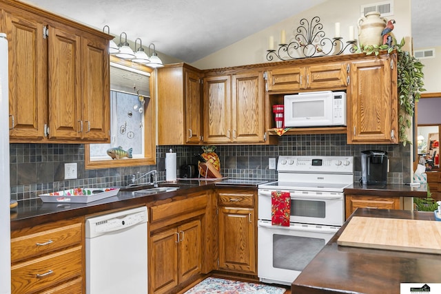 kitchen featuring brown cabinetry, dark countertops, white appliances, and visible vents