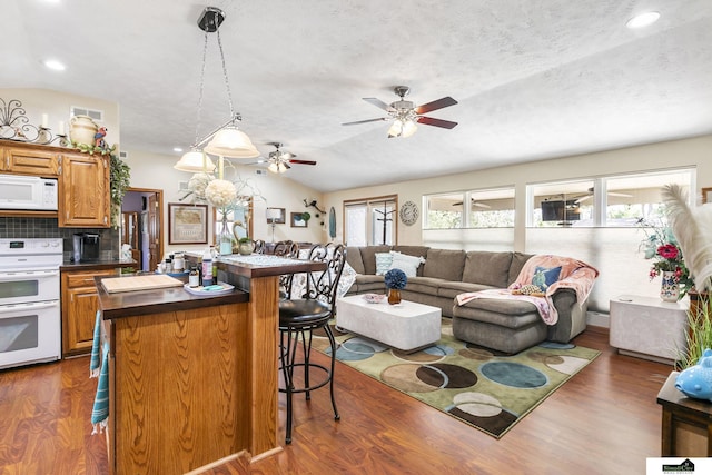 kitchen featuring white appliances, a breakfast bar, open floor plan, brown cabinetry, and dark countertops