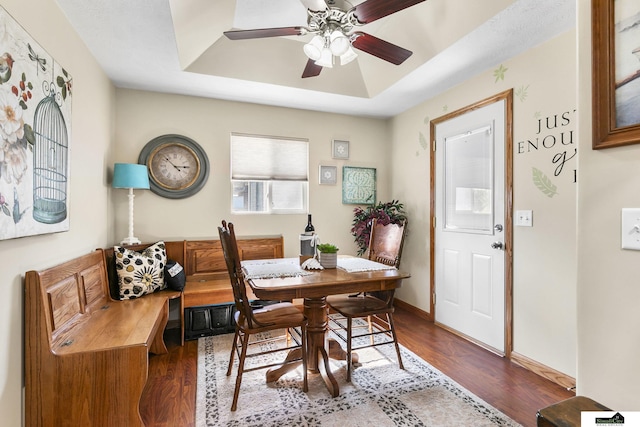 dining area with a ceiling fan, baseboards, a raised ceiling, and wood finished floors