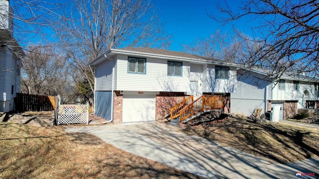 bi-level home featuring a garage, concrete driveway, brick siding, and fence