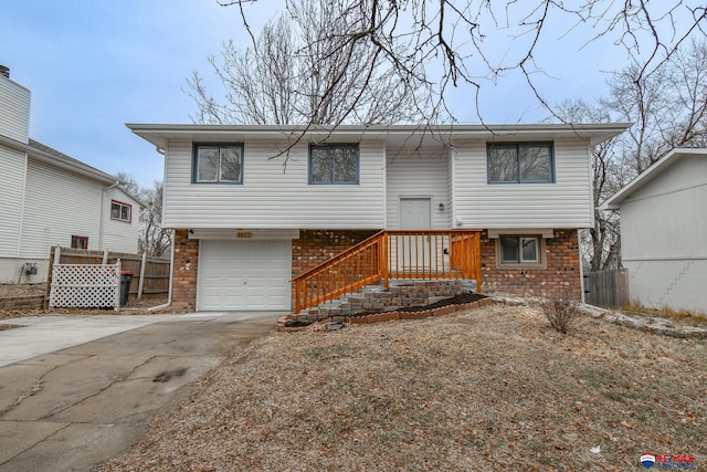 raised ranch featuring concrete driveway, brick siding, an attached garage, and fence