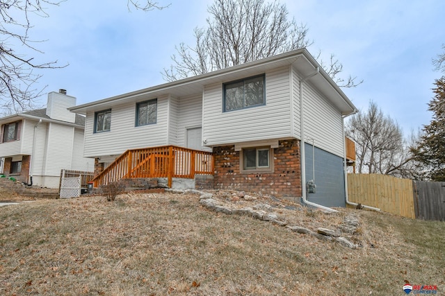 bi-level home featuring a deck, brick siding, a front yard, and fence