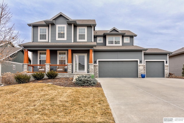 craftsman house with stone siding, a porch, concrete driveway, and a front yard